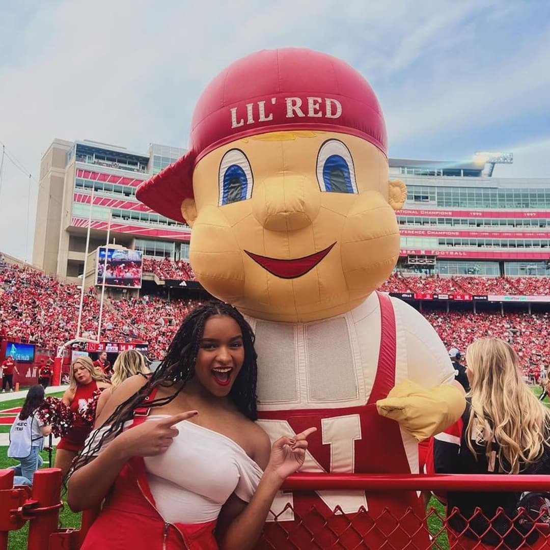 A Husker poses with and points to Lil' Red at Memorial Stadium.