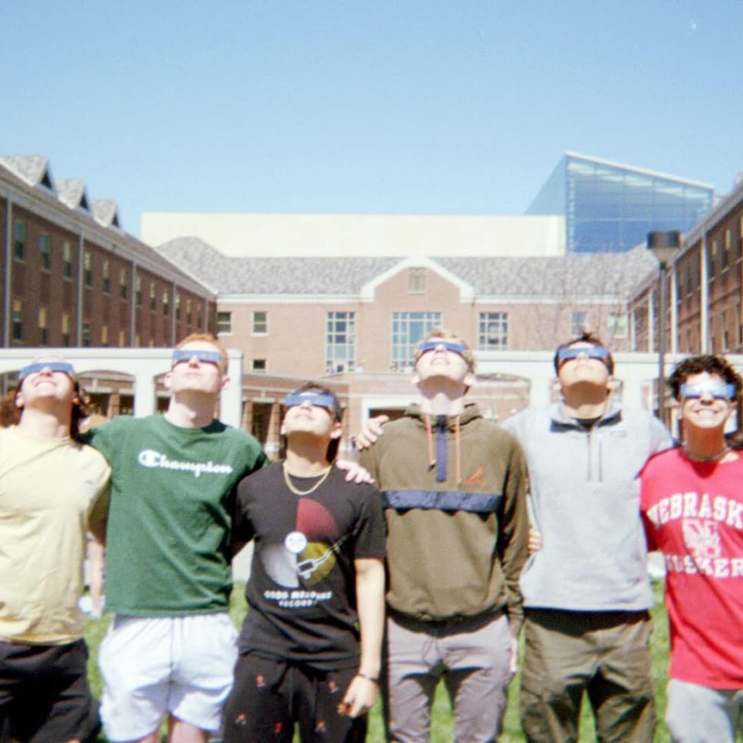 Six Huskers wearing eclipse glasses look up at the sky.