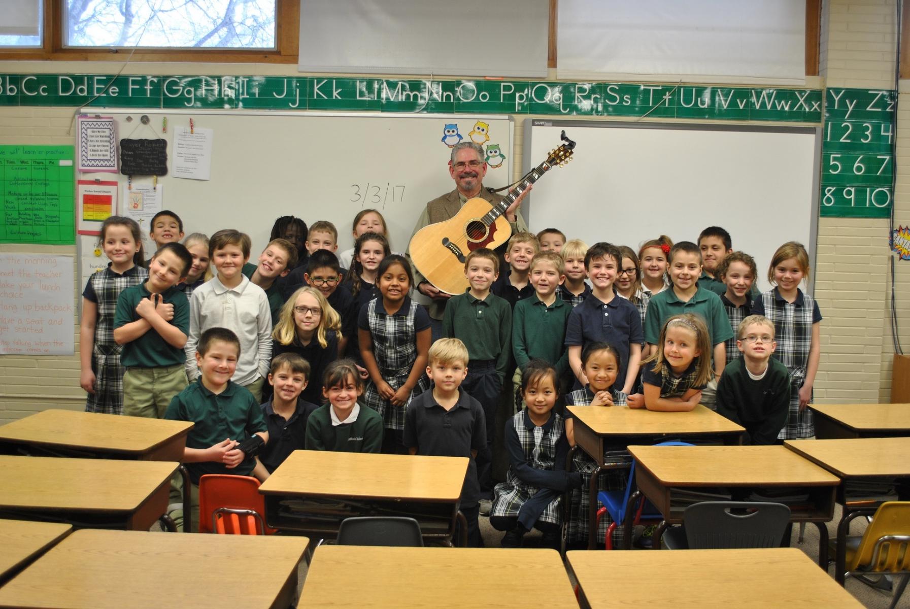 Steve Buhler and his guitar with students at Cathedral of the Risen Christ School