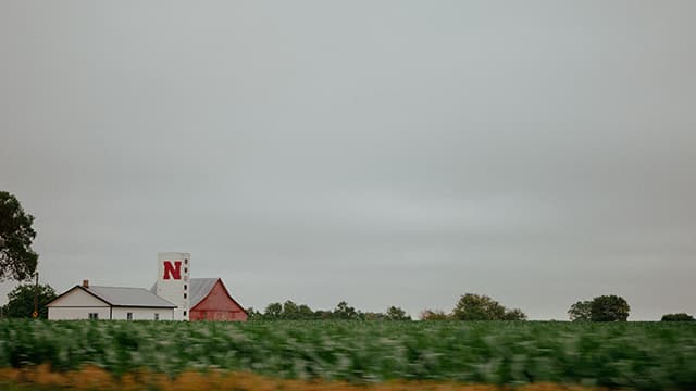 Mostly blue sky with farmland and buildings at the bottom of the frame. A white silo is painted with a red Nebraska N.