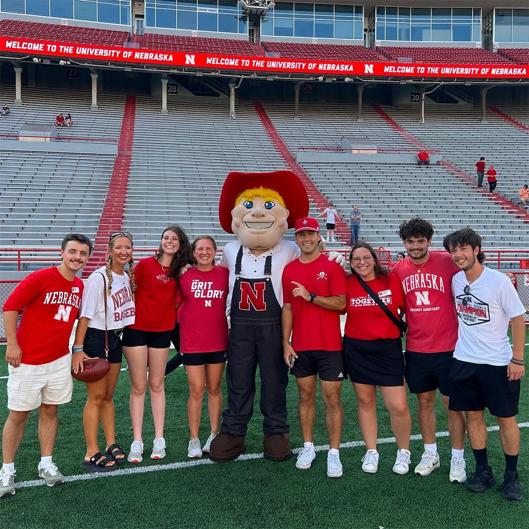 Eight Huskers pose with Herbie Husker on the field at Memorial Stadium.