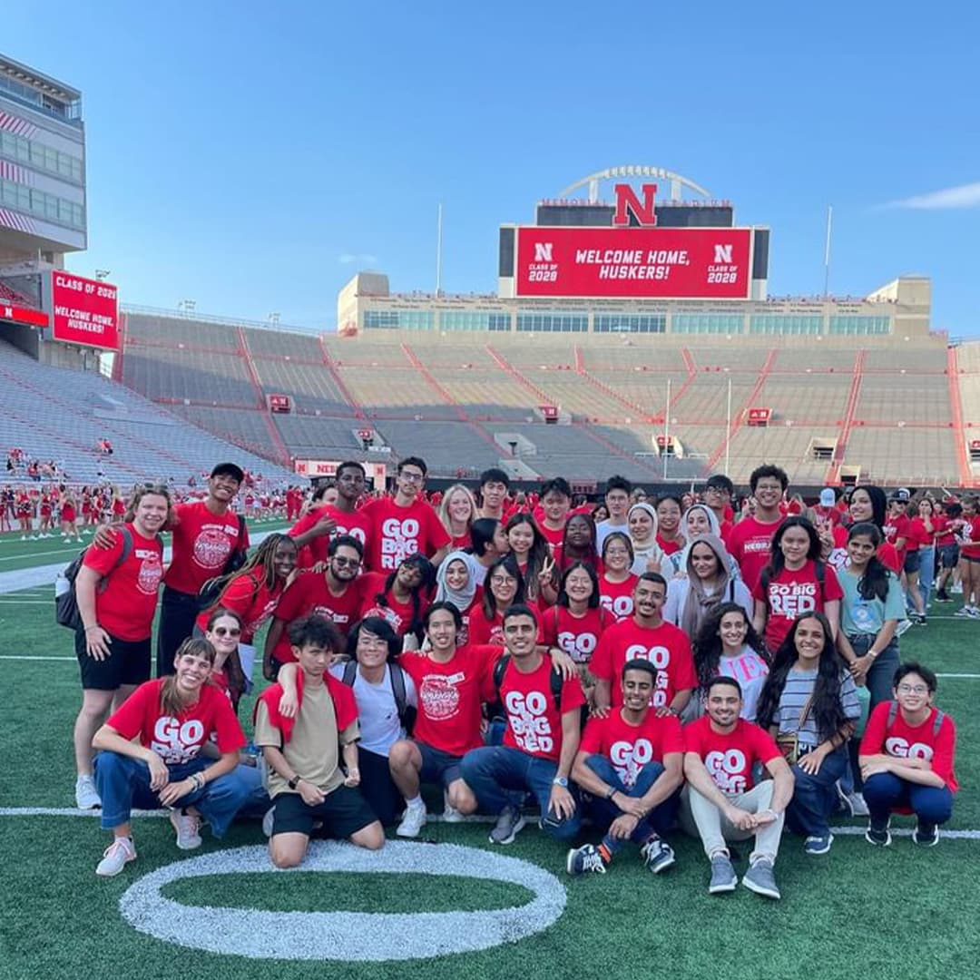 A large group of Huskers – some sitting, some standing – on the field at Memorial Stadium.