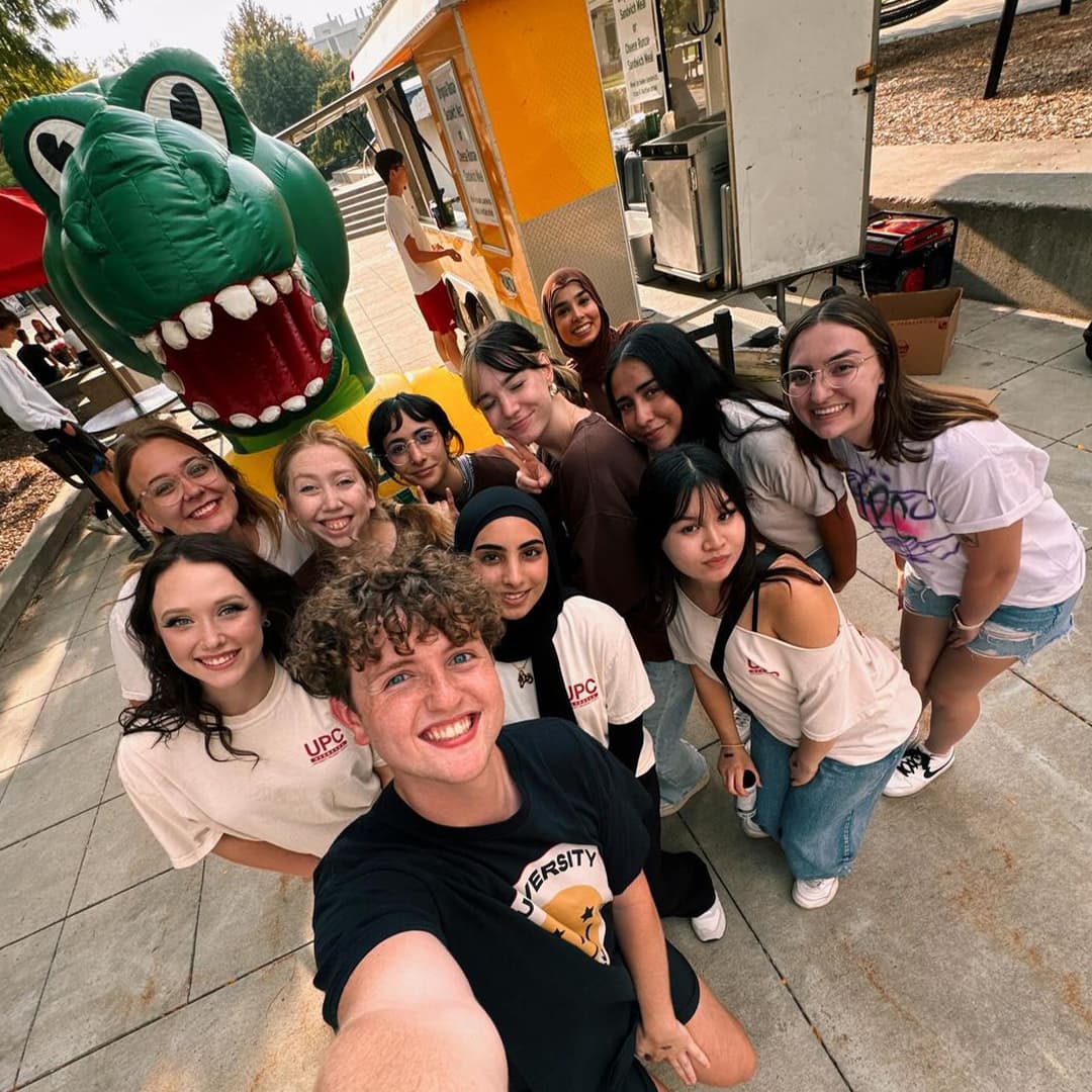 A group of eleven smiling Huskers take a selfie with Runza Rex.