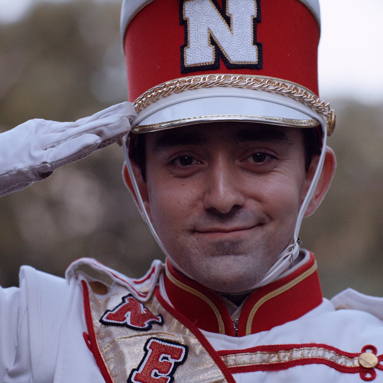 Jason Manzitto, wearing his Cornhusker Marching Band uniform, salutes the camera with a smile