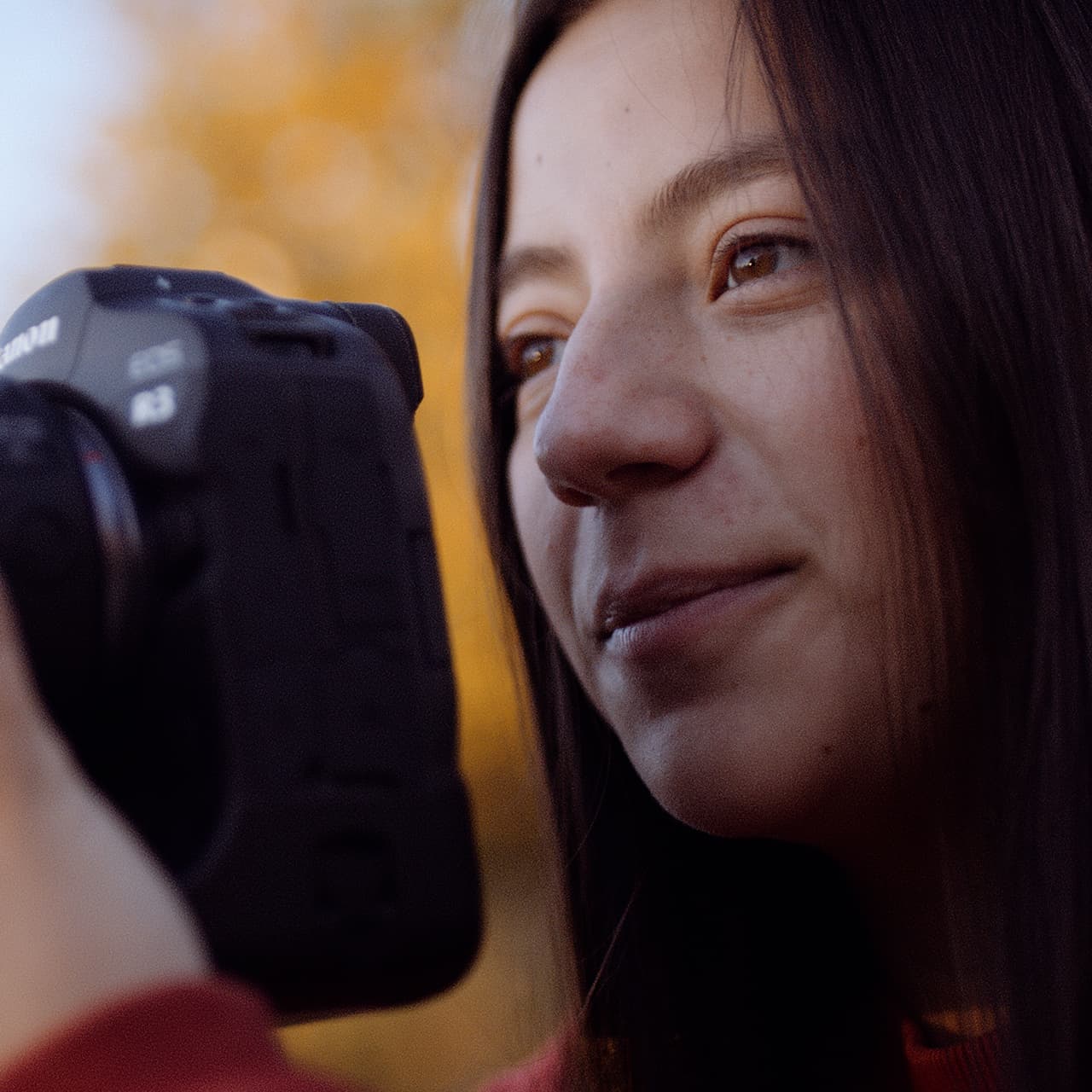 Sammy Smith looks through the viewfinder of a camera with fall foliage in the background