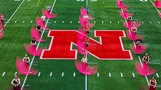 Members of the Cornhusker Marching Band Color Guard spin flags on the field of Memorial Stadium.