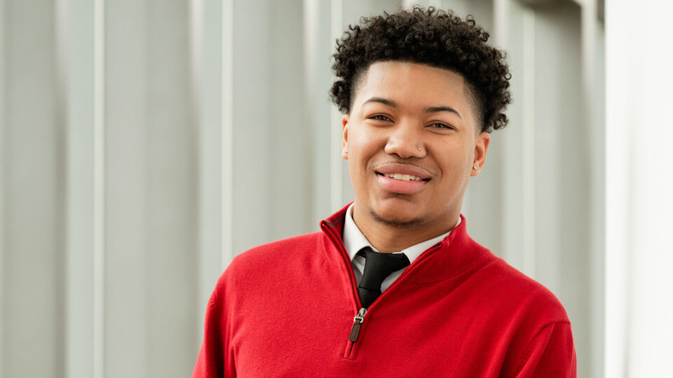 Student in red pullover sweater standing in building entryway