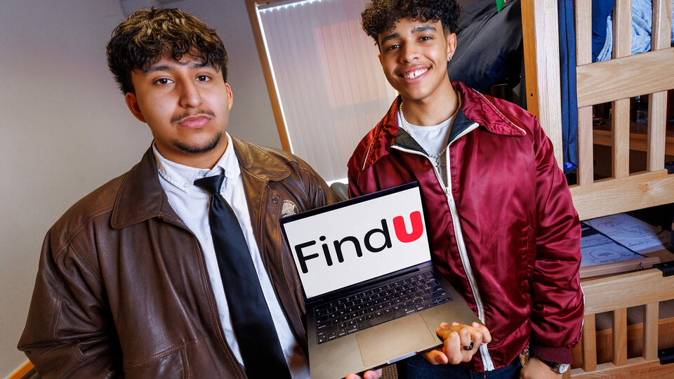 Students in dorm room holding laptop with application on it