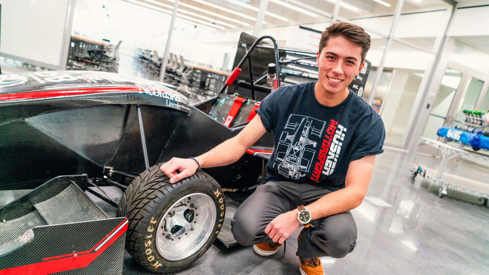 Student kneeling by racecar inside garage