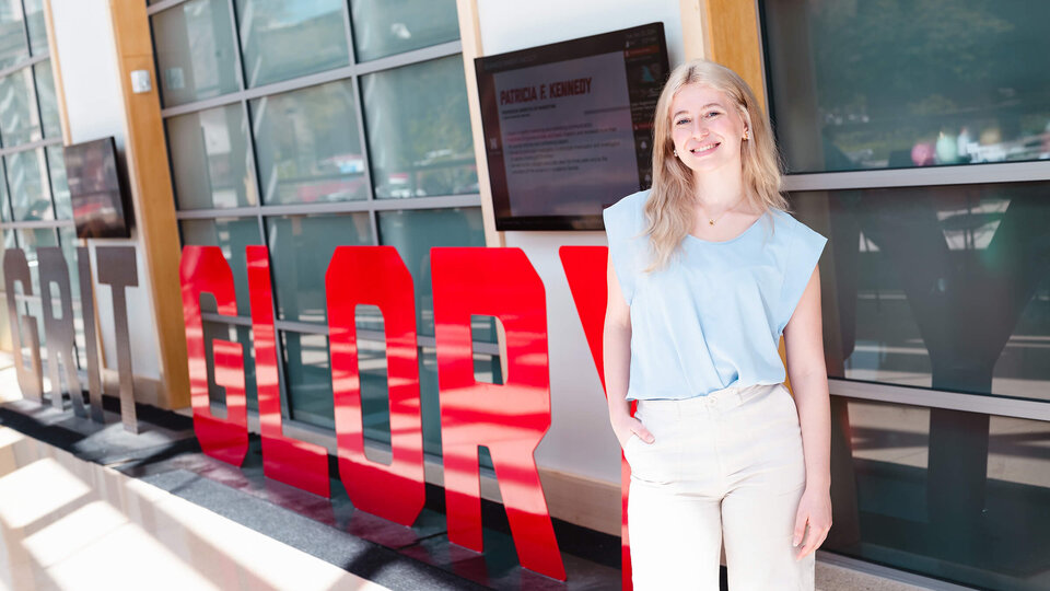 Student standing in front of Grit and Glory sculpture in College of Business