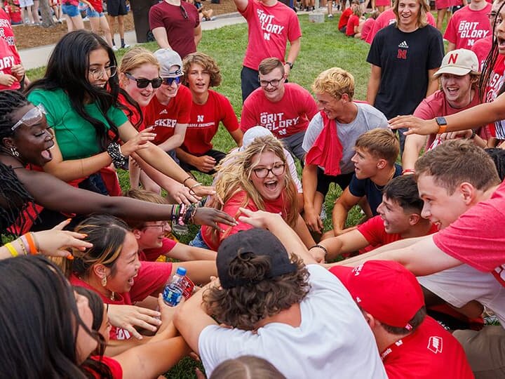 A large group of smiling Huskers put their hands into a huddle