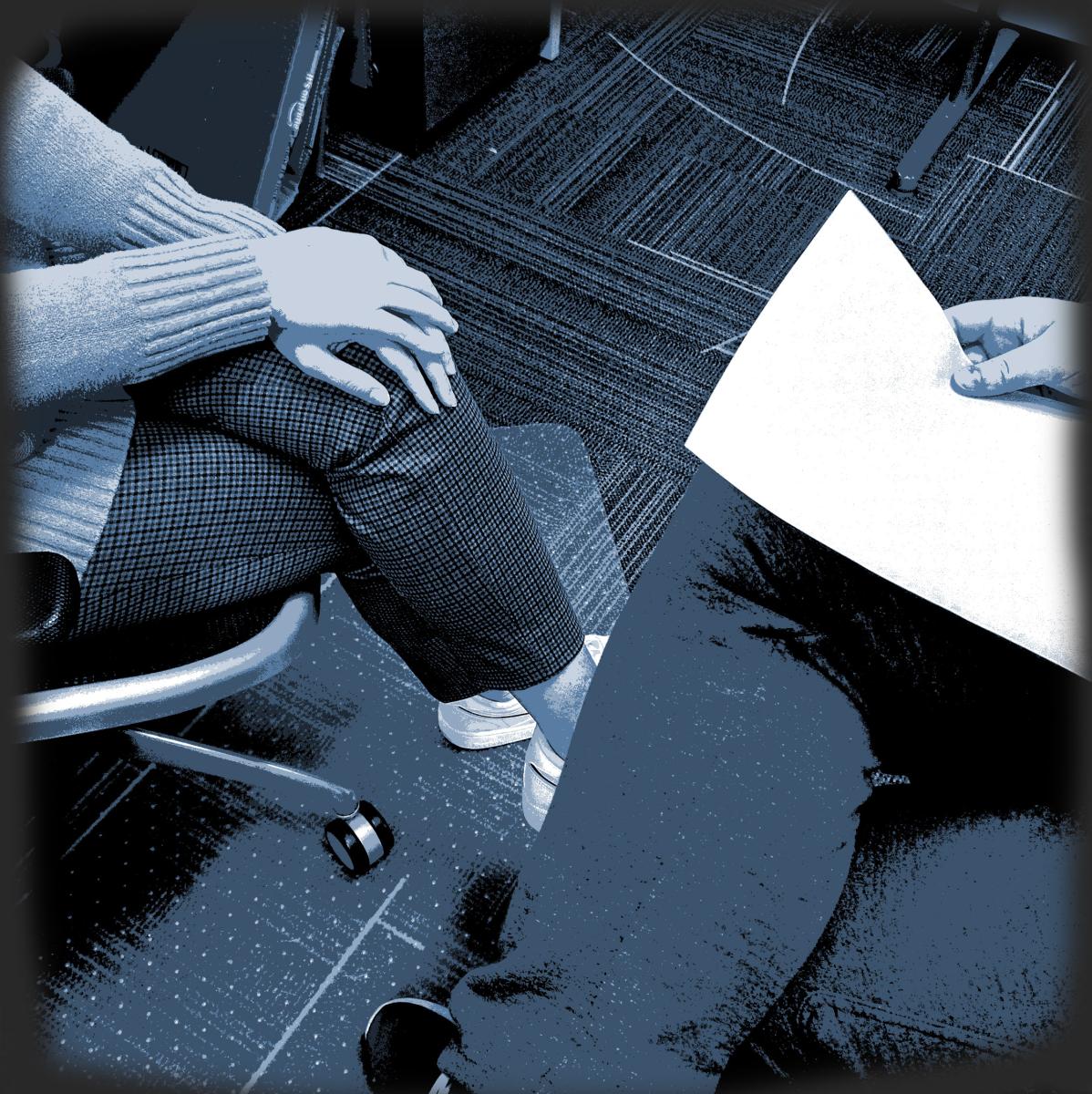Two people seated across from each other. Legs are crossed. One person is holding a piece of paper