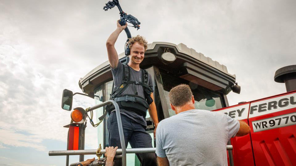 Student holding camera while standing on combine with gray sky in background