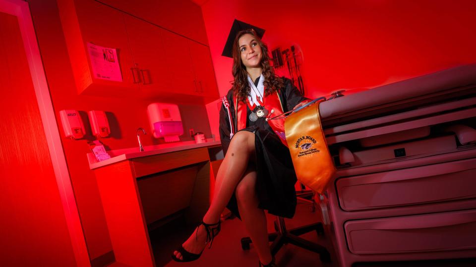 Student in cap and gown sitting on exam table with award ribbon